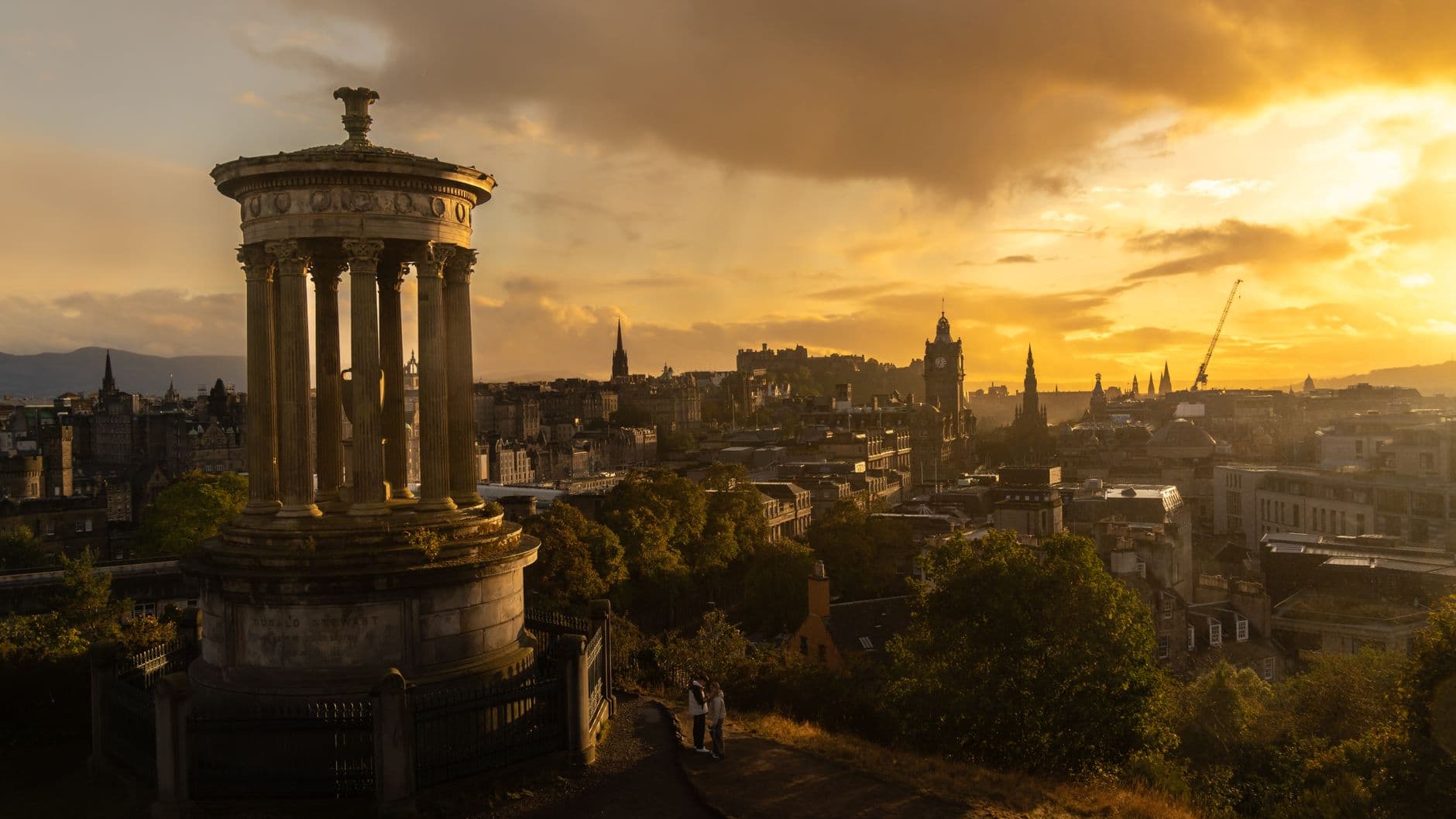 Dramatic sunset view of Edinburgh skyline from Calton Hill with Dugald Stewart Monument in the foreground.