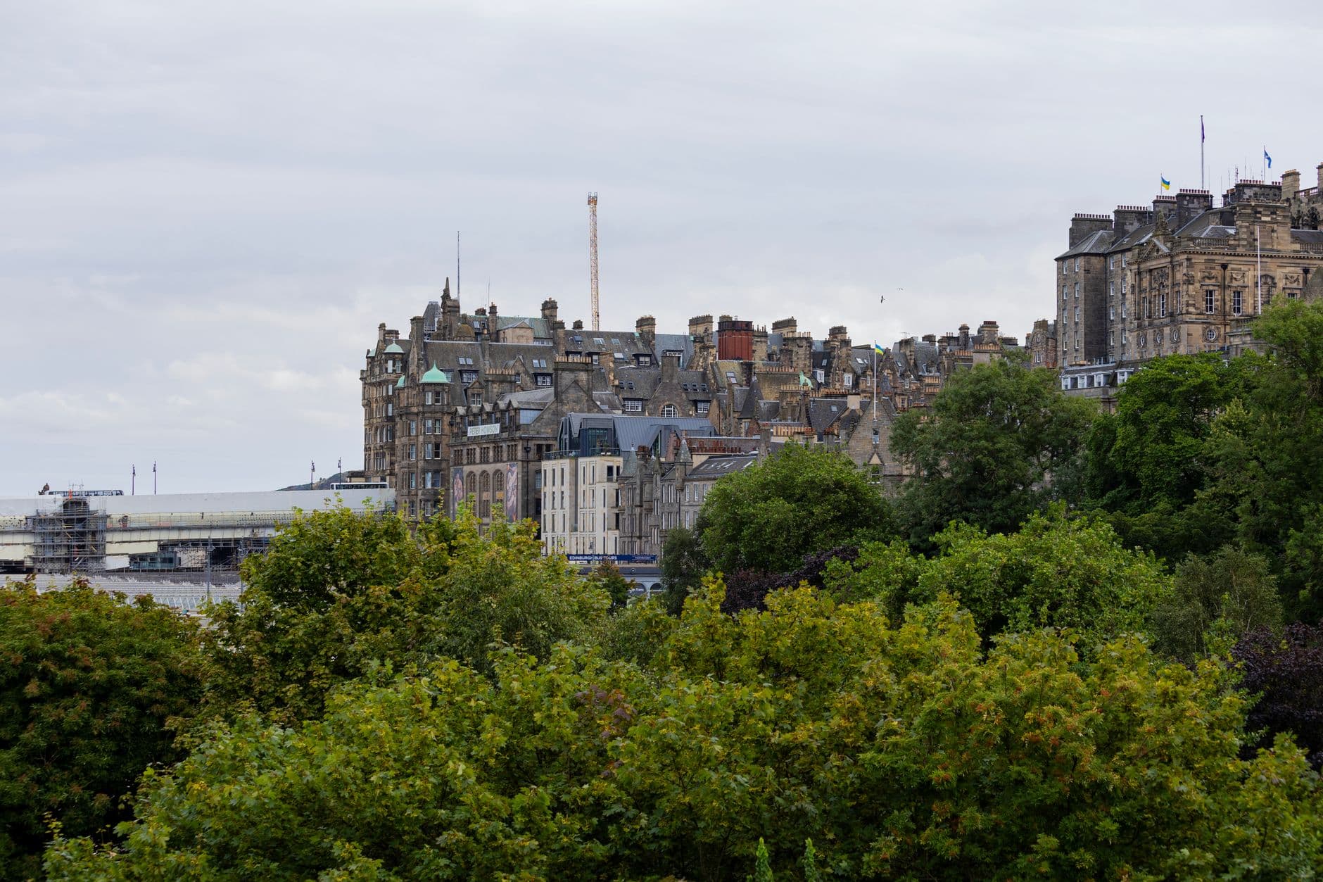 A scenic view of Edinburgh's iconic architecture surrounded by lush trees under a cloudy sky.
