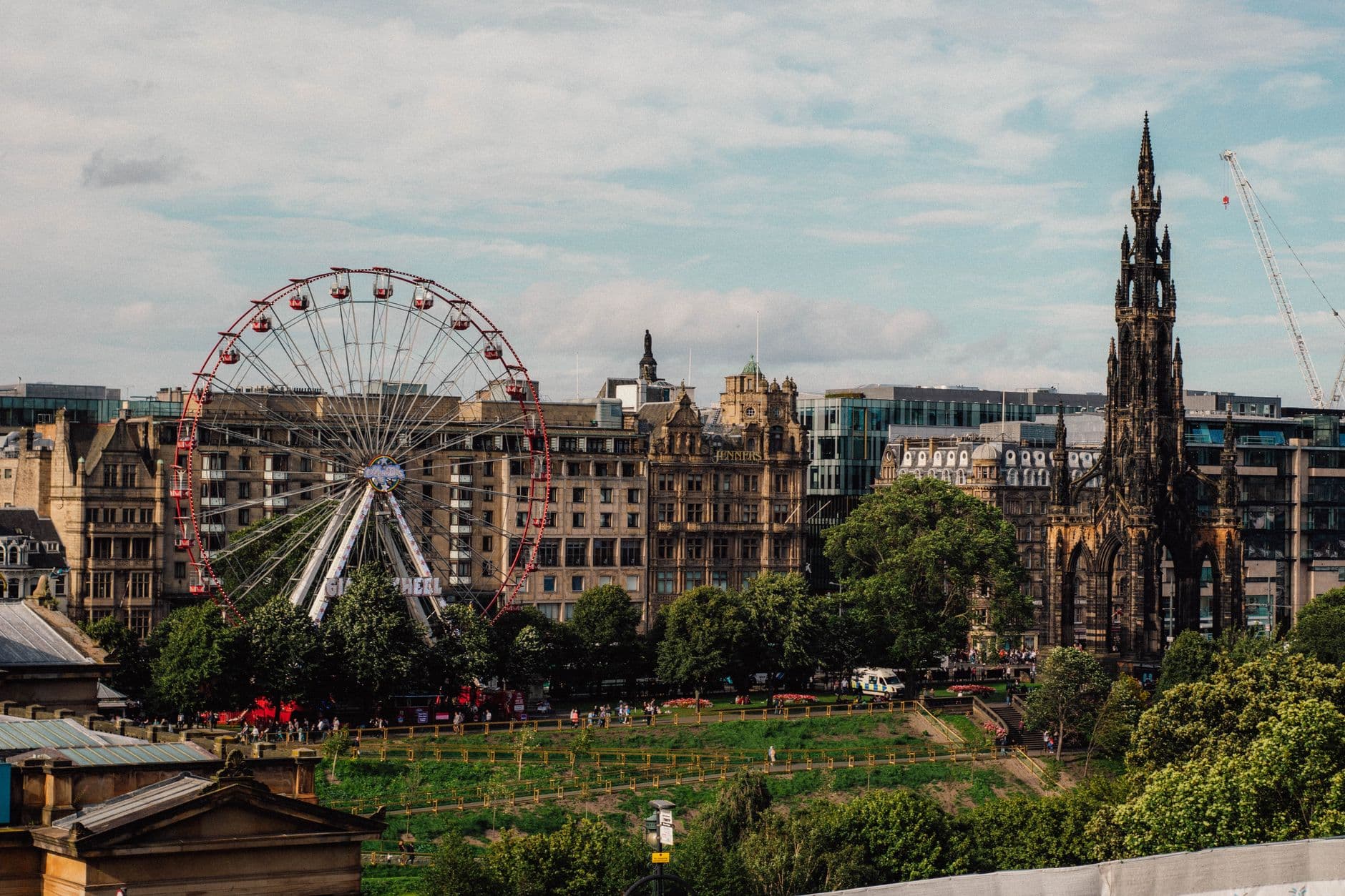 Scenic view of Edinburgh's iconic Ferris wheel and Scott Monument under a clear sky.